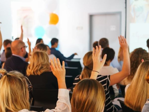 Participants of the conference vote and signal the speaker with their hands up in a special audience with a projector and screen.
